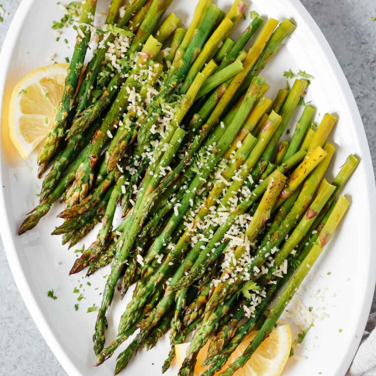 Easy roasted asparagus on a serving platter topped with parmesan cheese and lemon wedges.