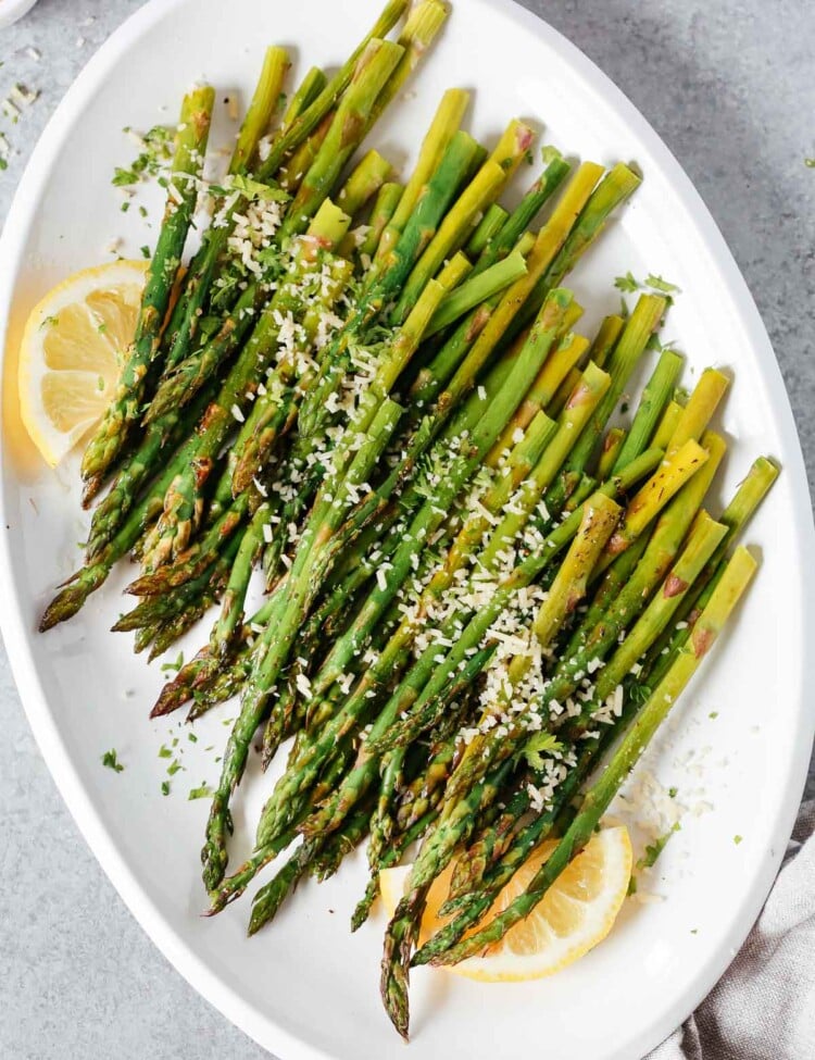 Easy roasted asparagus on a serving platter topped with parmesan cheese and lemon wedges.