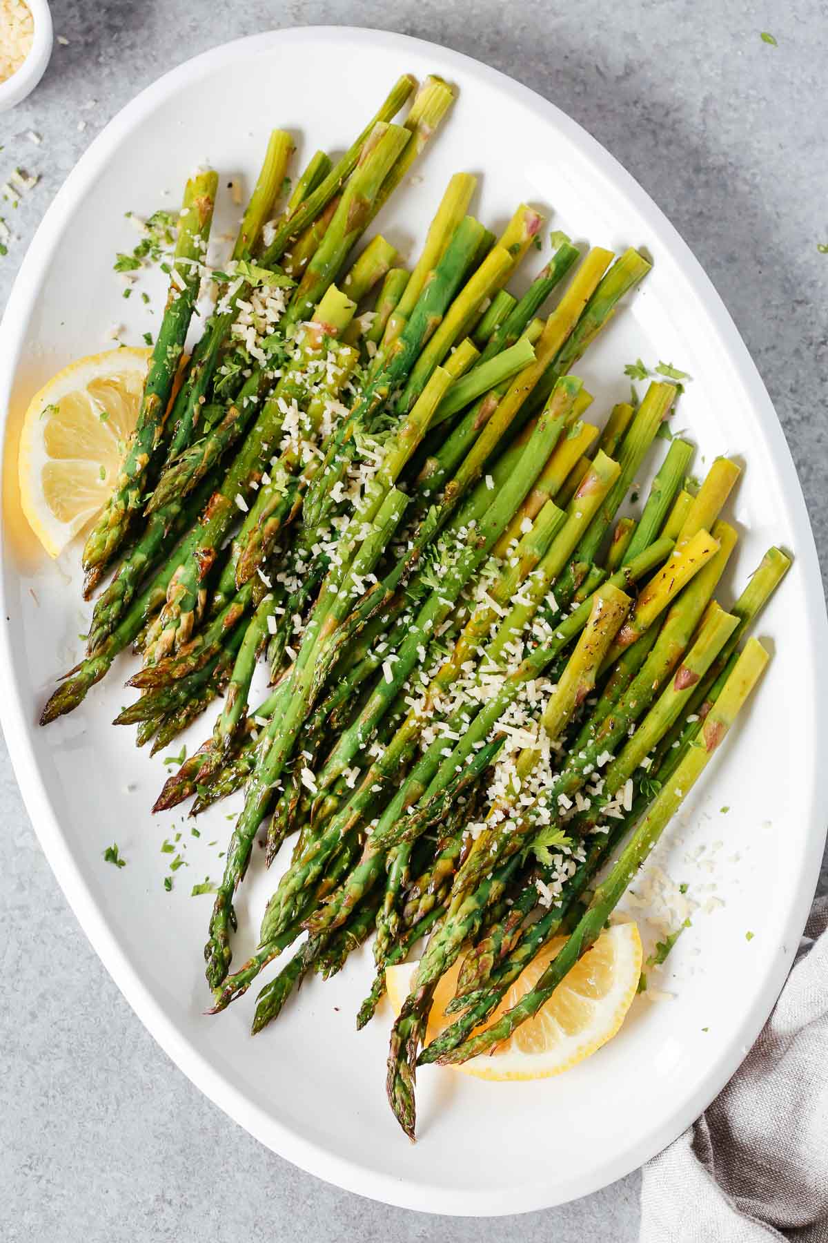 Roasted asparagus on a serving platter topped with parmesan cheese and lemon wedges.