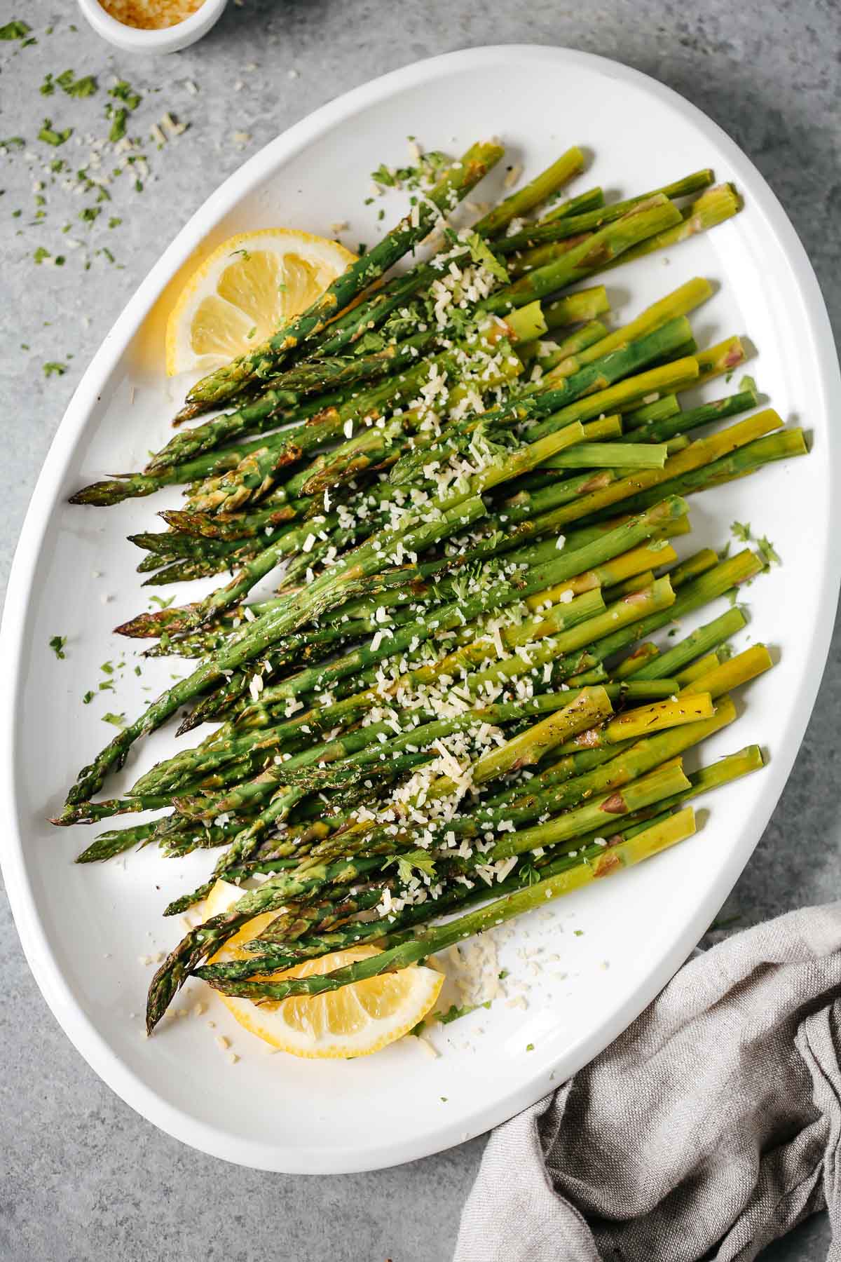 Easy roasted asparagus on a white plate topped with parmesan cheese and lemon wedges.