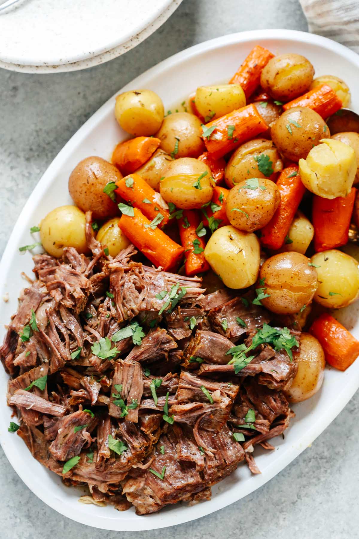 Pressure cooker pot roast recipe in a white serving plate with carrots and potatoes.