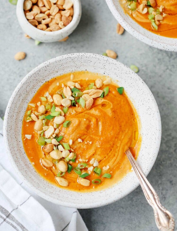 A bowl of carrot soup with green onion and peanut garnished on top.