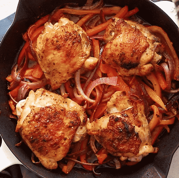Overhead view of cast iron skillet containing chicken thighs, slices of onions and bell pepper