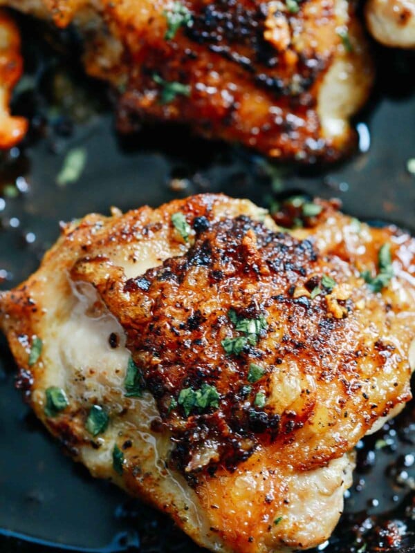 close of up crispy chicken thighs in a pan topped with fresh parsley
