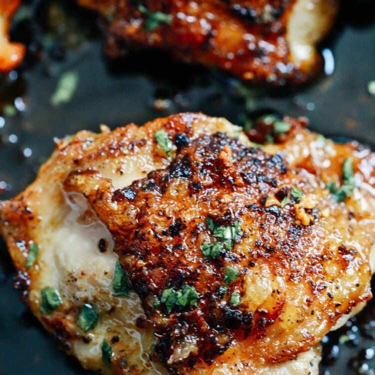 close of up crispy chicken thighs in a pan topped with fresh parsley