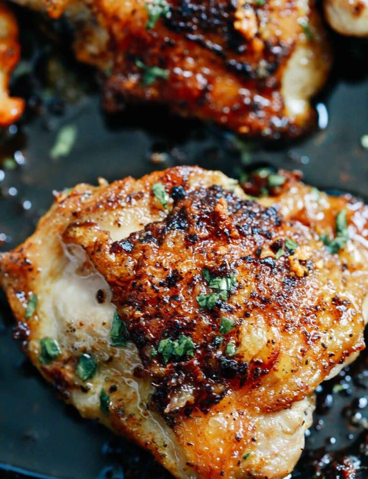 close of up crispy chicken thighs in a pan topped with fresh parsley