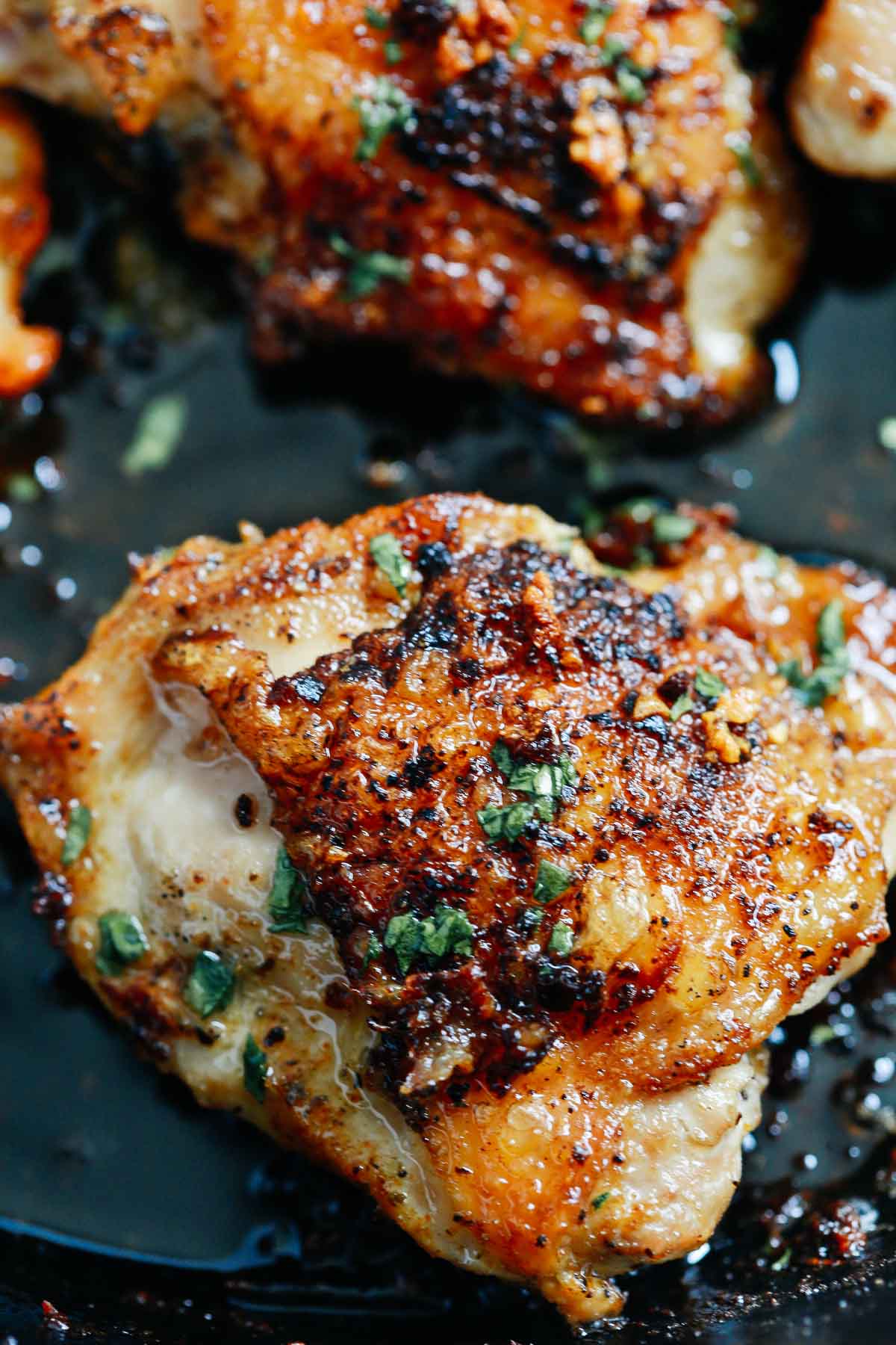 close of up crispy chicken thighs in a cast iron skillet topped with fresh parsley