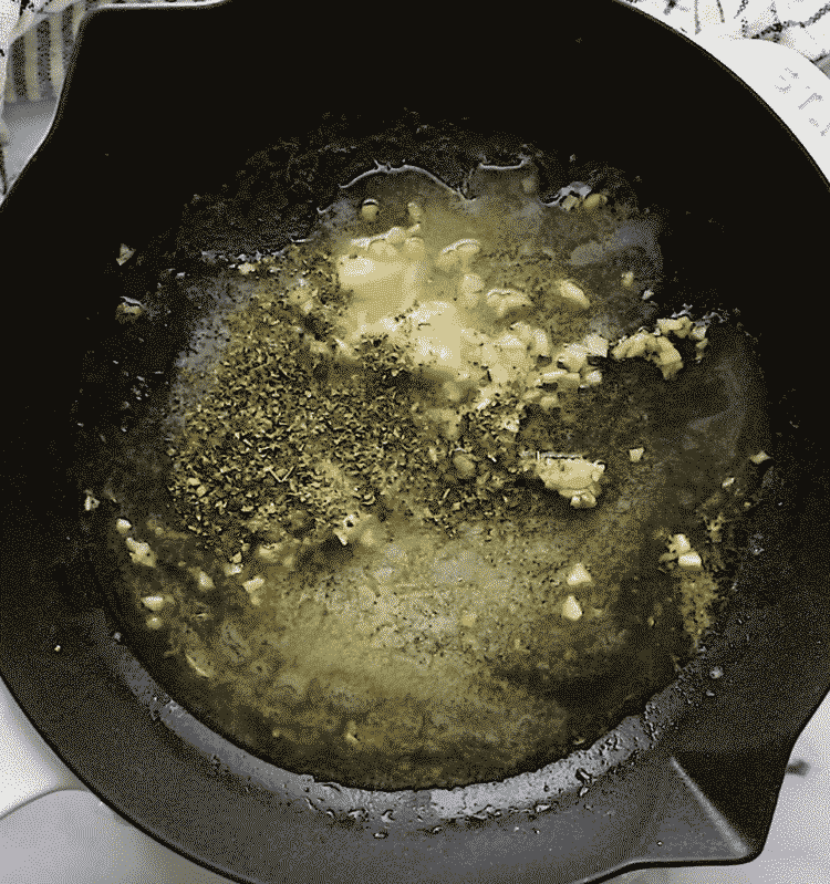 overhead view of cast iron skillet containing melted butter, garlic, lemon juice and spices.