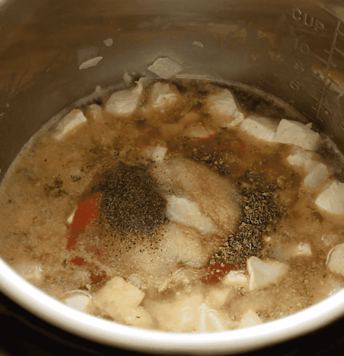 Cubed chicken cooks in a pot with broth, visible seasonings like ground pepper, salt, and herbs floating on top. Measurement markings are on the pots side above the simmering mixture.