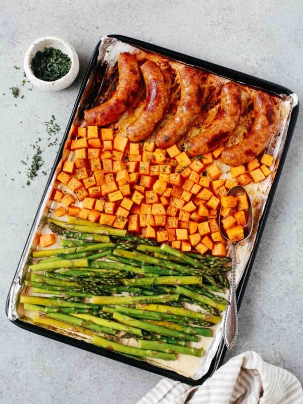 Overhead view of a sheet pan containing cooked sausage, sweet potatoes, and asparagus.