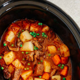 A slow cooker filled with Slow Cooker Beef Stew, featuring chunks of beef, potatoes, carrots, and green peas in a rich broth. Text above reads Slow Cooker Beef Stew.