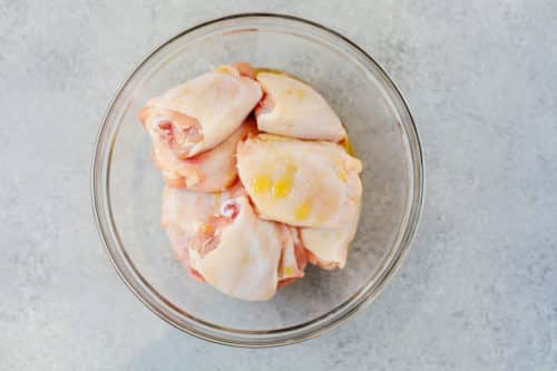 overhead view of raw chicken thighs inside of a glass bowl