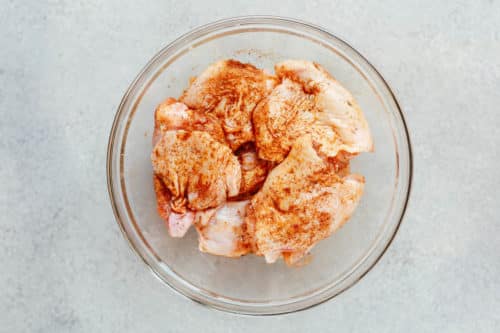 overhead view of raw chicken thighs with spices inside of a glass bowl