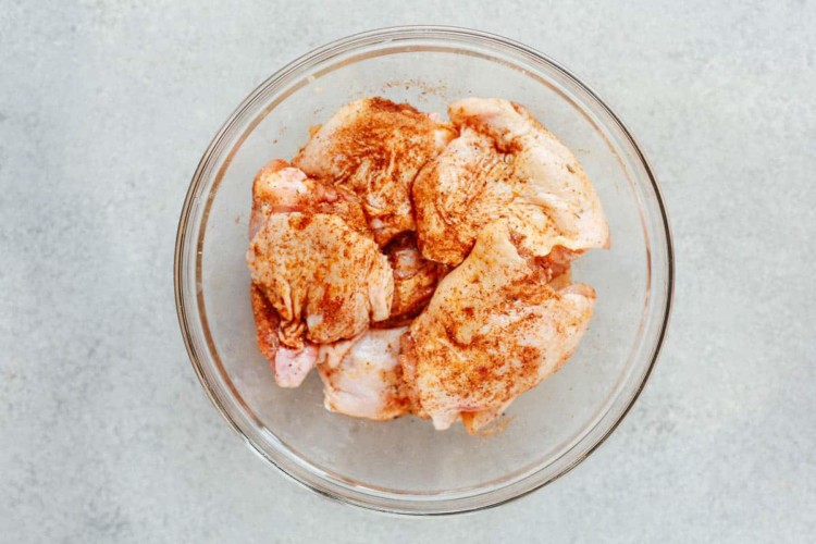 overhead view of raw chicken thighs with spices inside of a glass bowl