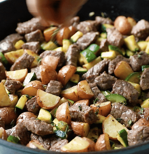 closeup of diced potatoes, beef and zucchini in a cast iron skillet