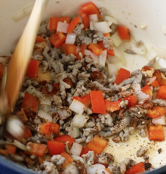 Chopped onions, carrots, and ground meat are being sautéed in a pot, with a wooden spoon stirring the mixture.