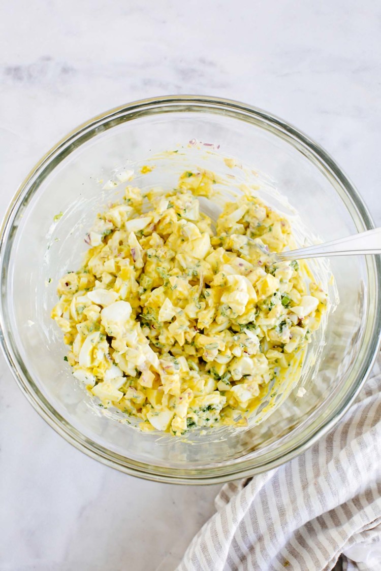 overhead view of a glass bowl of egg salad with a spoon inside