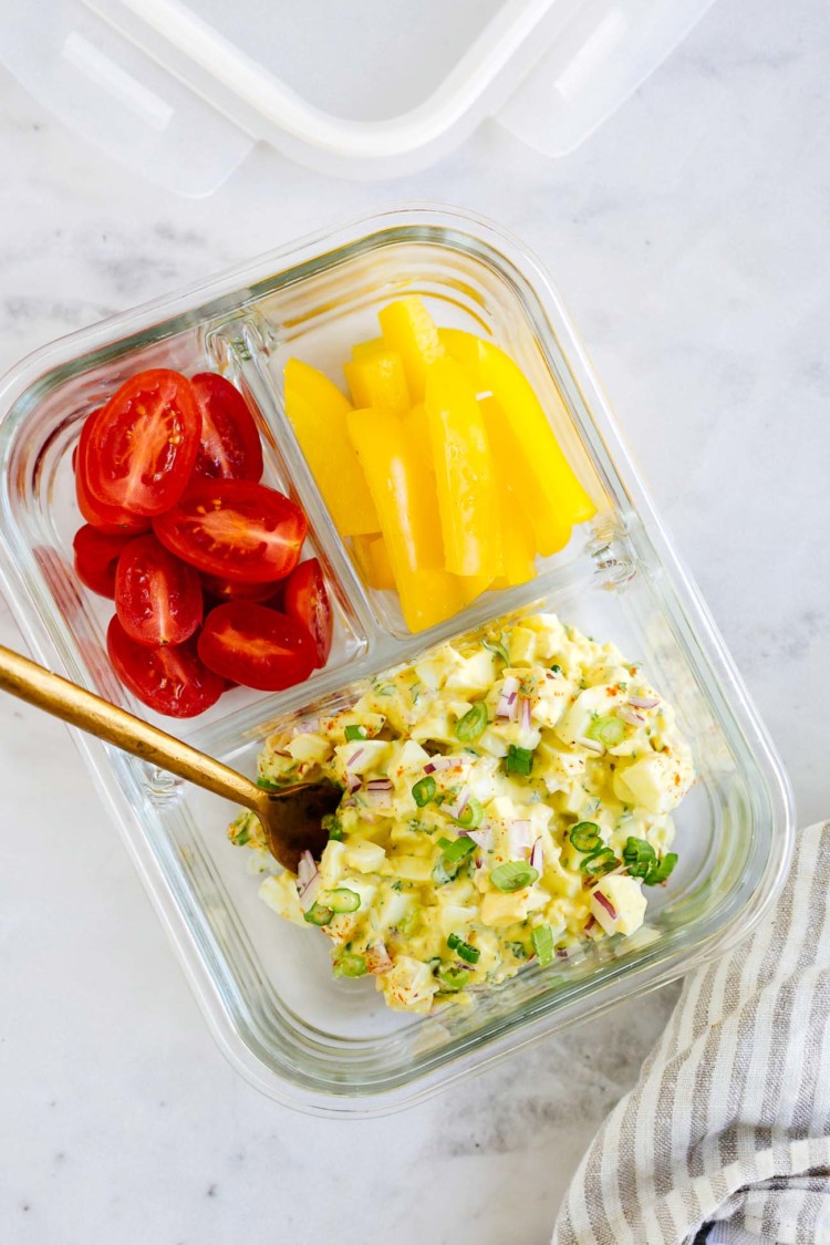 overhead view of a glass container with cherry tomatoes, bell pepper and egg salad