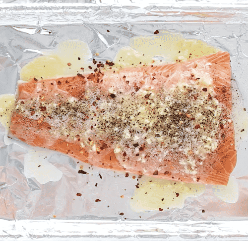 overhead view of salmon with melted butter in a baking sheet