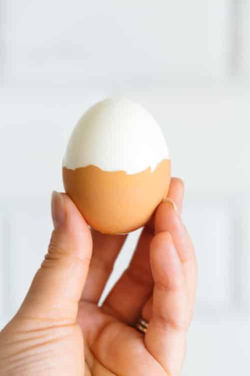 A hand holding up a half peeled hard boiled egg