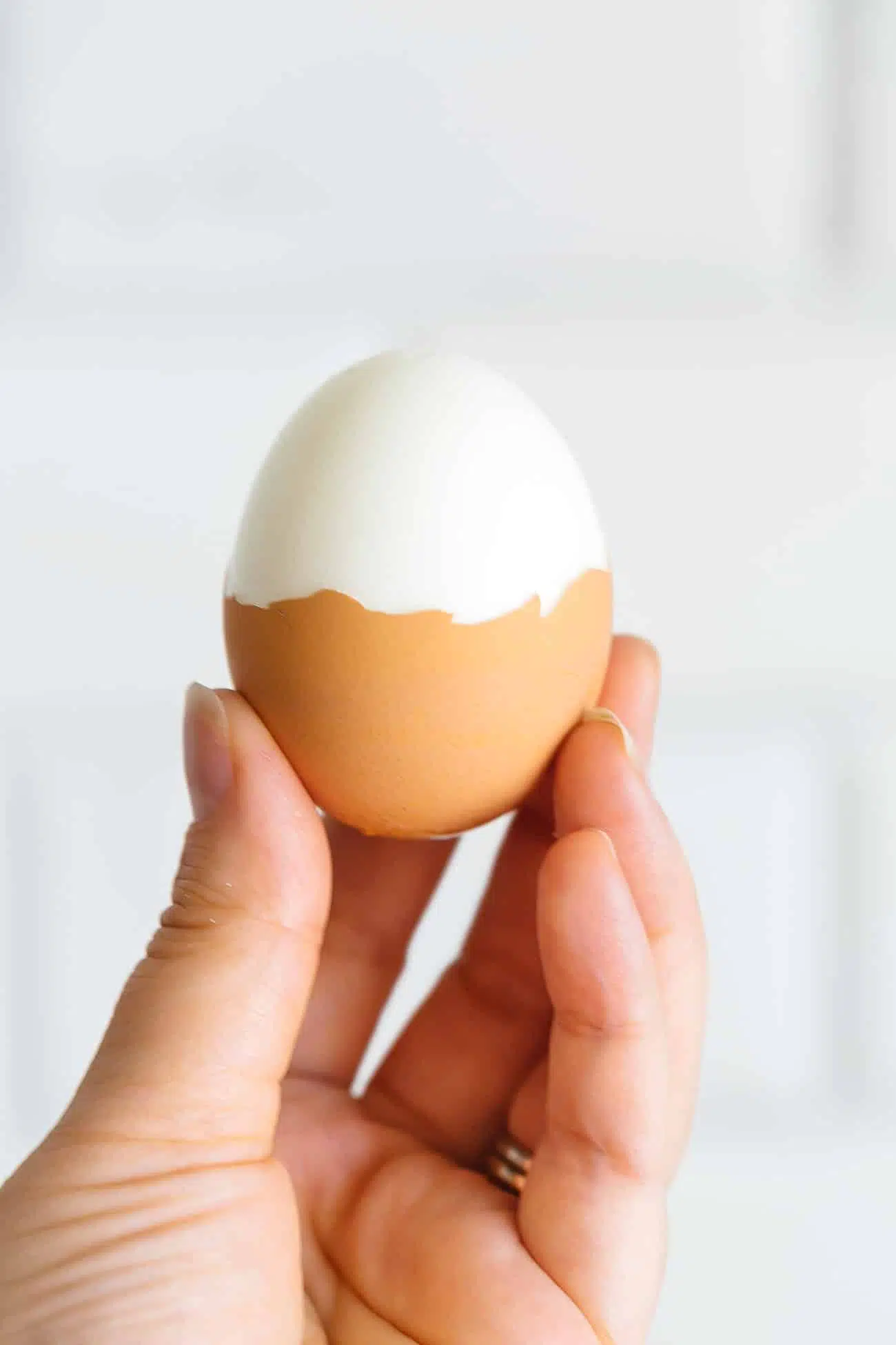 A hand holding a half peeled hard boiled egg.
