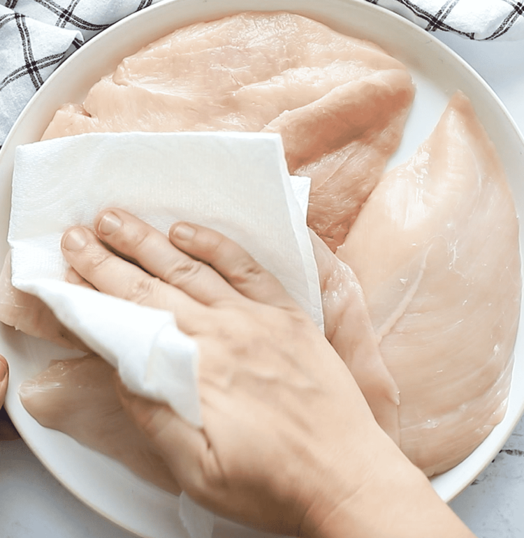overhead view of chicken breast being patted with a paper towel.