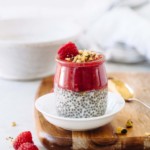 A jar of chia seed pudding with raspberry puree, raspberry, and pistachios on top.