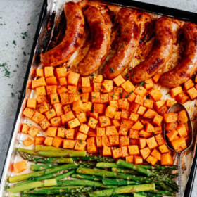 A sheet pan featuring sausage with sweet potato, alongside roasted asparagus, all arranged in neat rows. A serving spoon rests invitingly on the flavorful sweet potatoes.