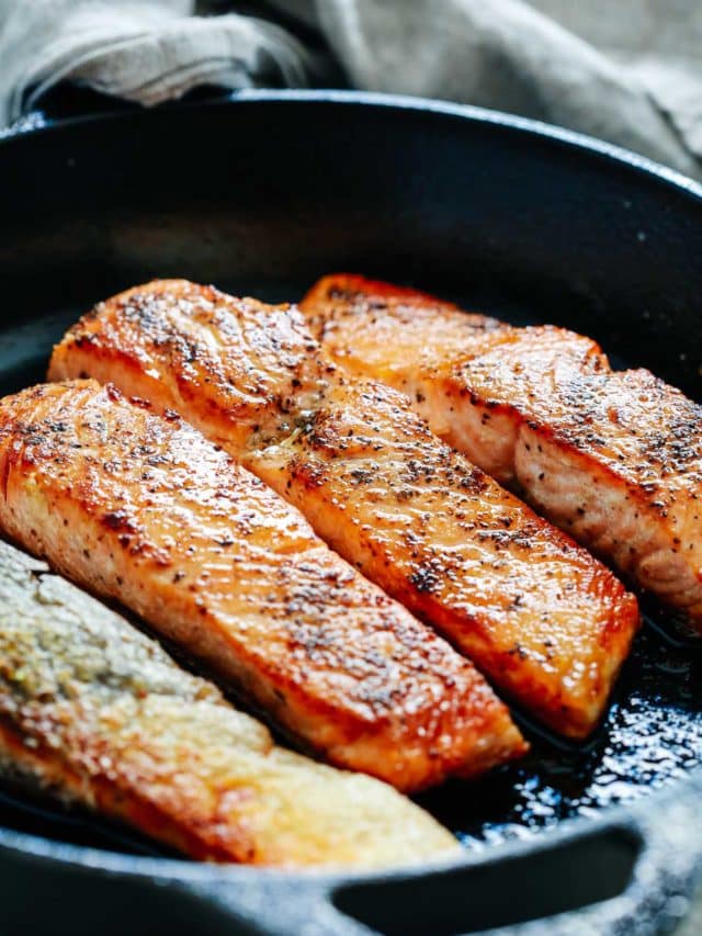 Close-up of 4 salmon fillets in a cast-iron skillet.