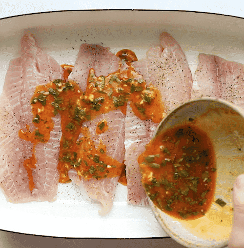 overhead view of a baking sheet containing tilapia fillets and melted butter