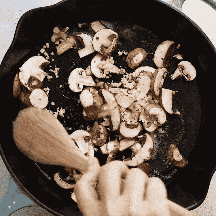 overhead view of cast iron containing mushroom, garlic and butter