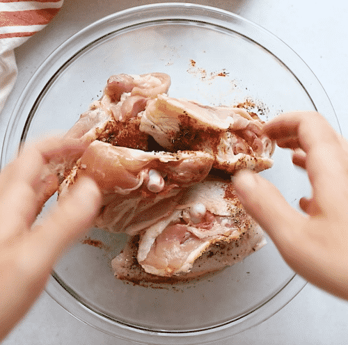 overhead view of a glass bowl containing seasoned chicken thighs