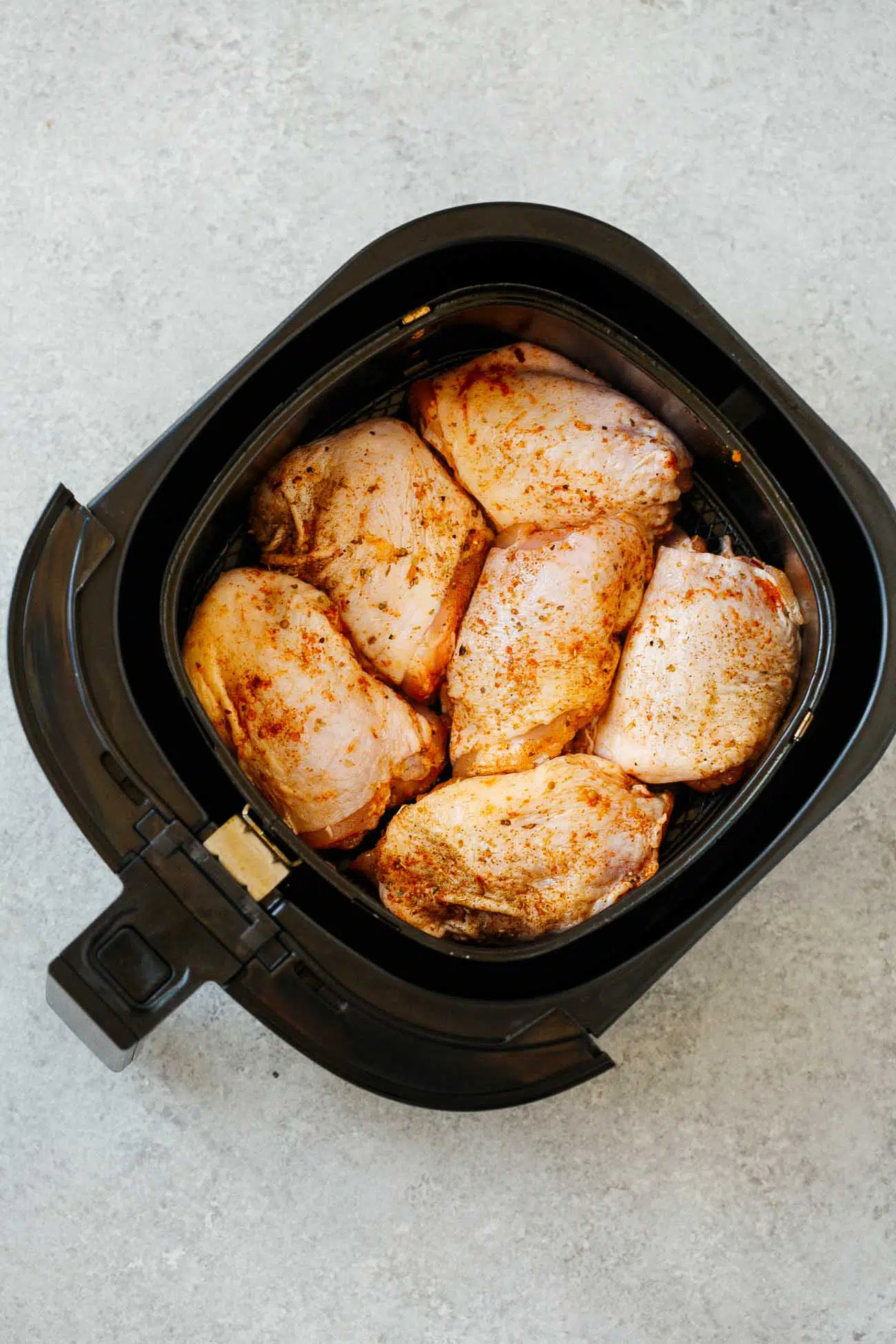 overhead view of raw chicken thighs inside of an air fryer bowl.