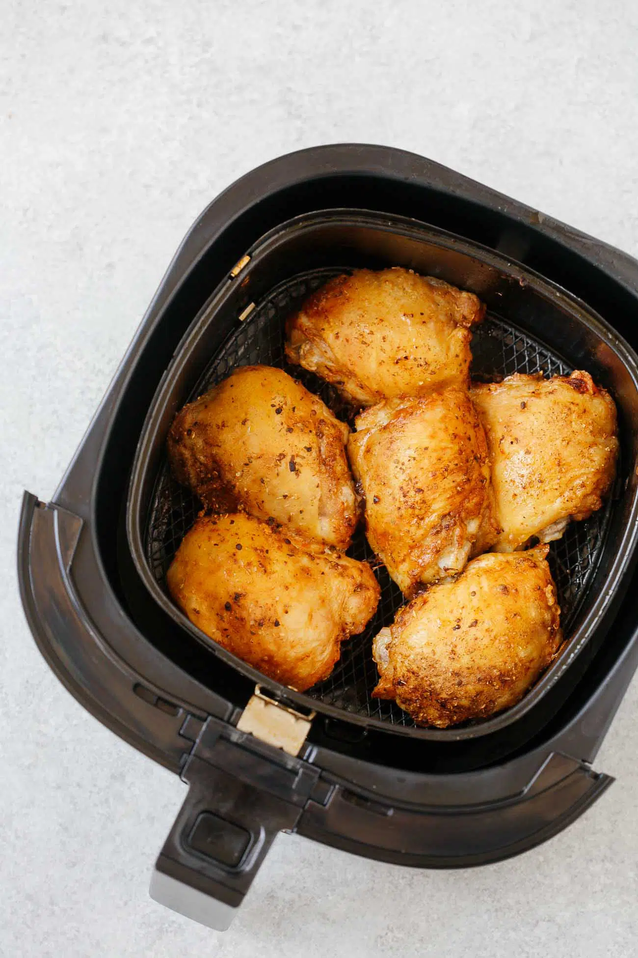 overhead view of cooked chicken thighs inside of an air fryer basket.