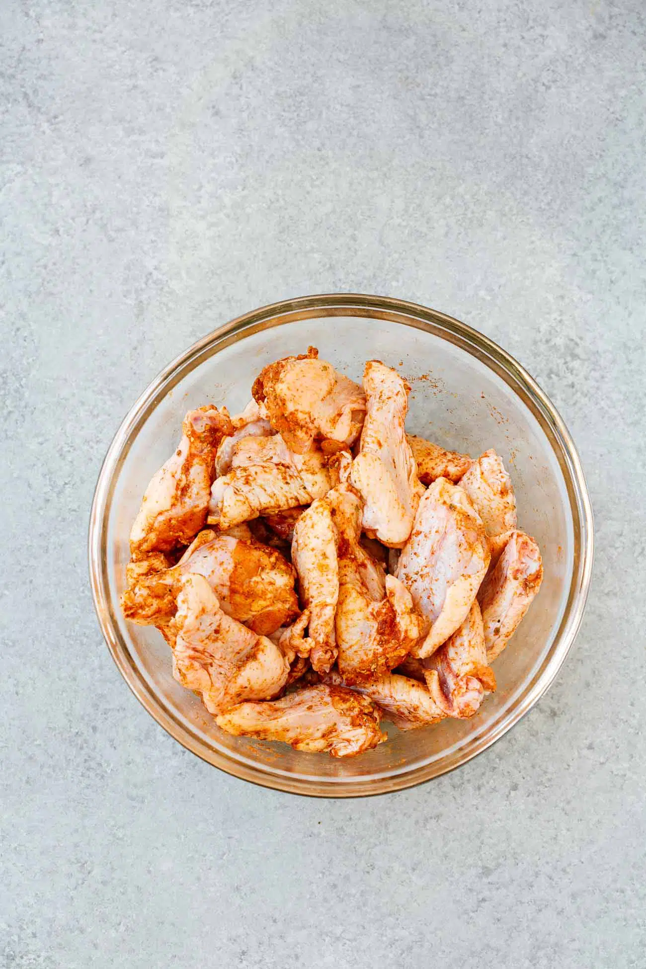 overhead view of a glass bowl containing raw chicken wings.