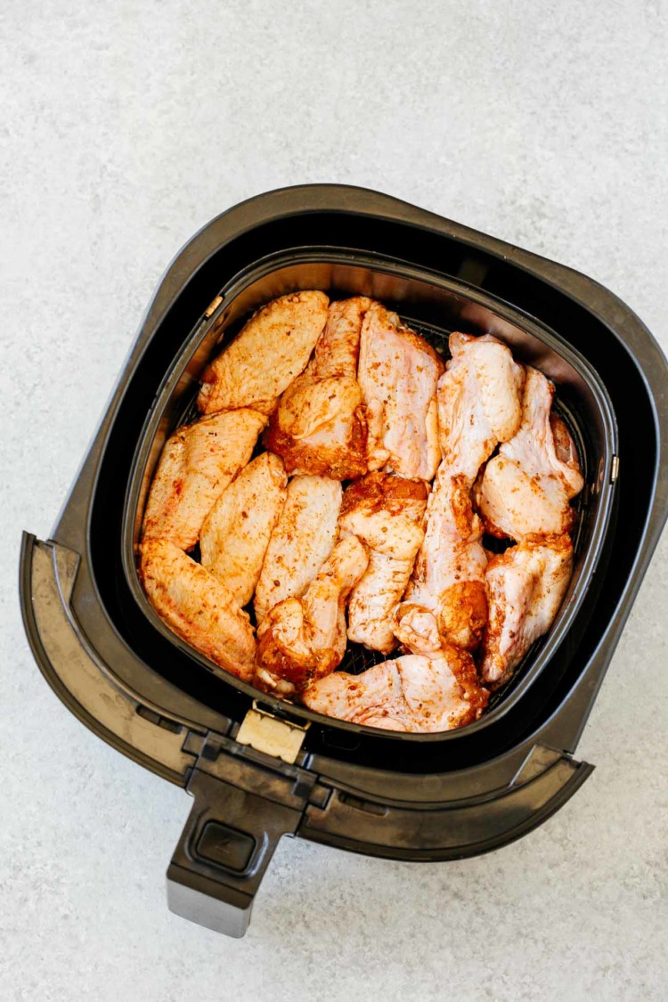 overhead view of an air fryer basket containing raw chicken wings