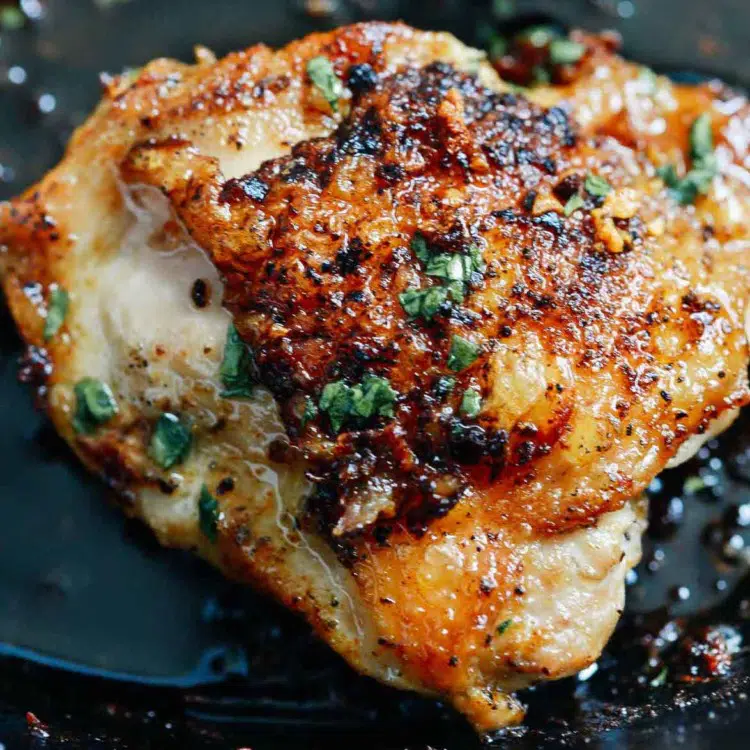 close up of chicken thighs in butter sauce inside of a cast iron skillet