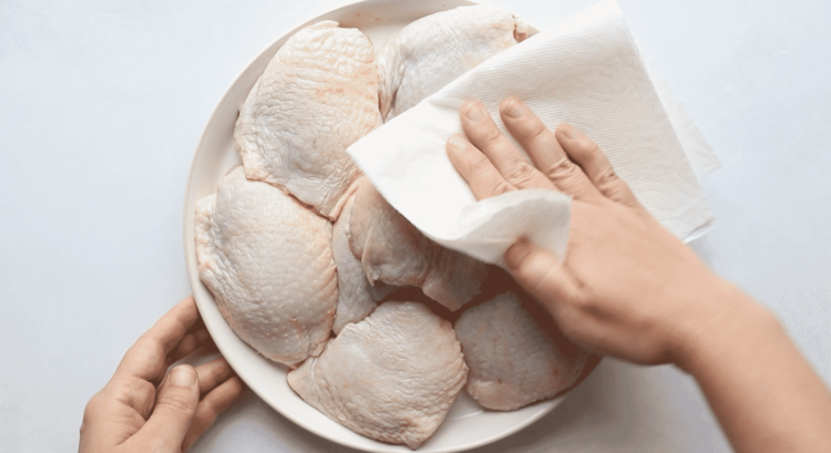 overhead view of a white plate with chicken thighs being petted with paper towel