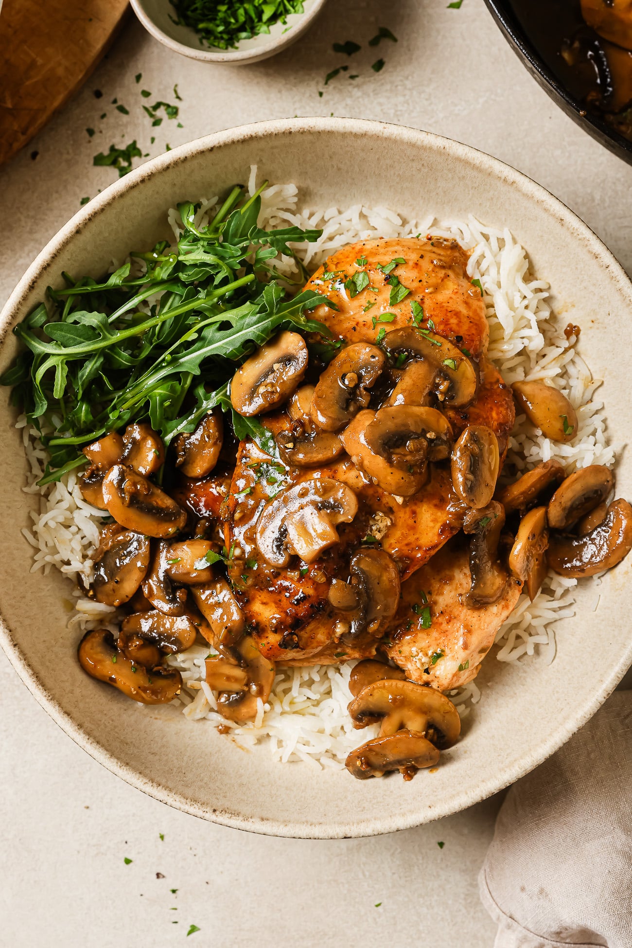 A bowl of white rice topped with flavorful chicken and mushroom, fresh arugula, and grilled chicken breasts, garnished with chopped parsley.
