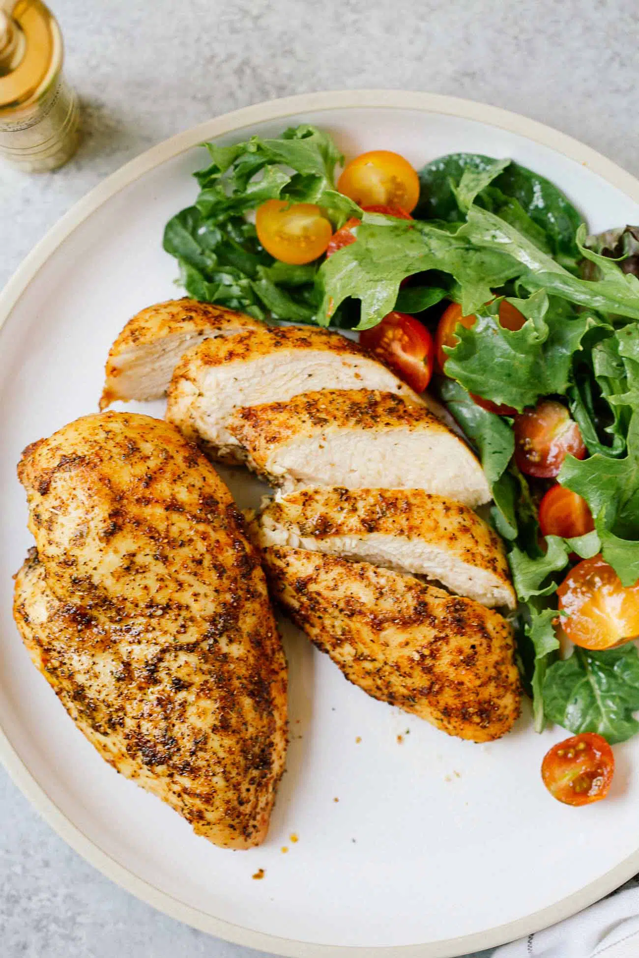 A plate with two chicken breasts, one sliced, beside a salad.