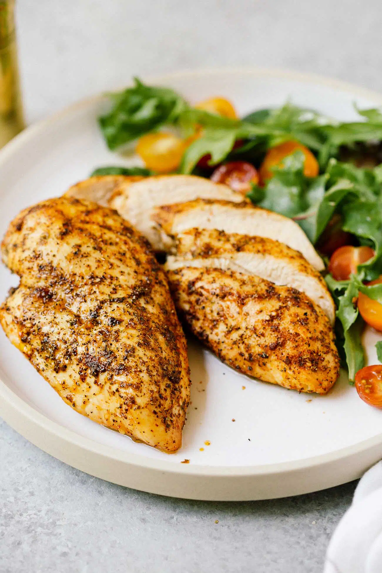 A plate with two air fryer chicken breasts. and a green salad with cherry tomatoes.