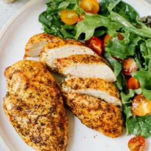 overhead view of chicken breast on a white plate with a green salad