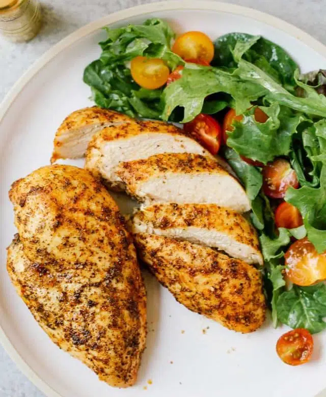 overhead view of chicken breast on a white plate with a green salad
