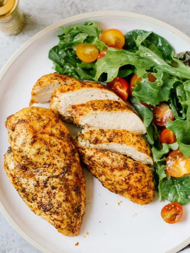 overhead view of chicken breast on a white plate with a green salad