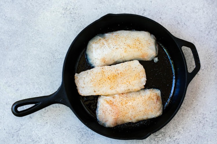 overhead view of raw halibut fish in a cast iron skillet