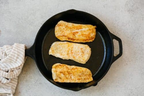 overhead view of cooked halibut fish in a cast iron skillet