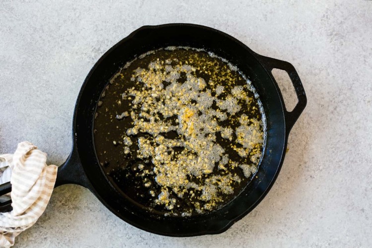 overhead view of melted butter and chopped garlic in a cast iron skillet