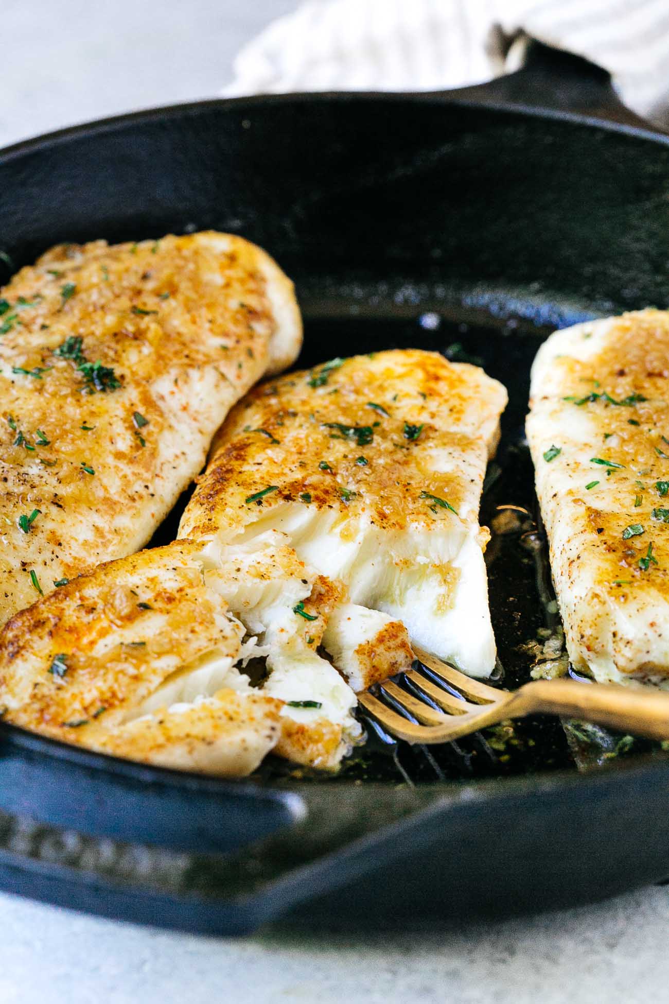 closeup of flaky garlic butter halibut fish in a cast iron skillet