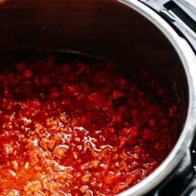 A close-up of Instant Pot Meat Sauce cooking in an Instant Pot, with a rich red color and chunks of meat visible. The words Instant Pot Meat Sauce appear at the top.