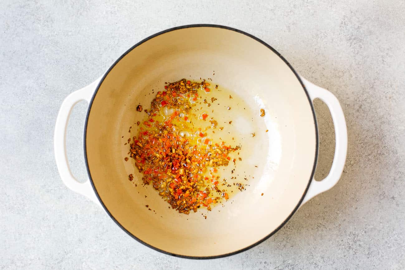 Chopped onions, peppers, and spices sizzling in oil at the bottom of a large white pot on a light countertop—a delicious foundation for an authentic Brazilian Fish Stew.